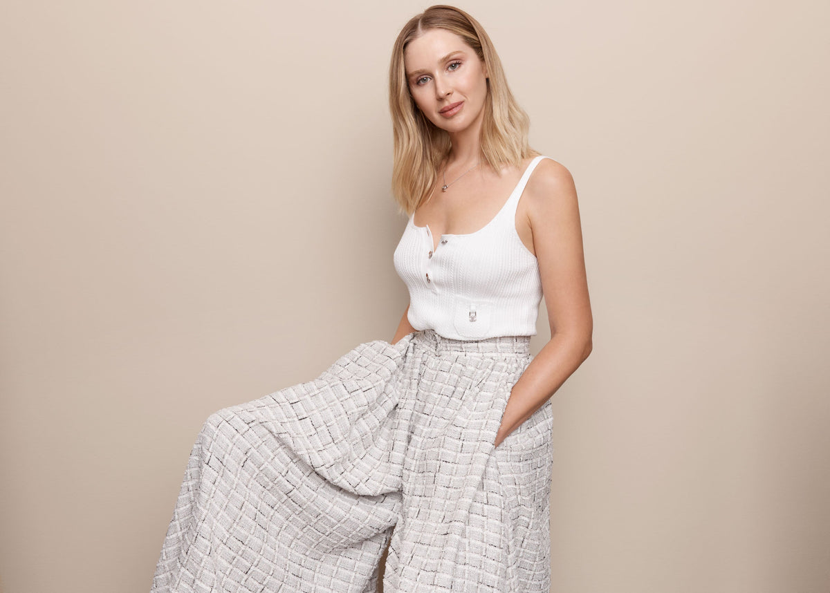 Melanie Grant in a white sleeveless top and wide-leg trousers against a beige backdrop.