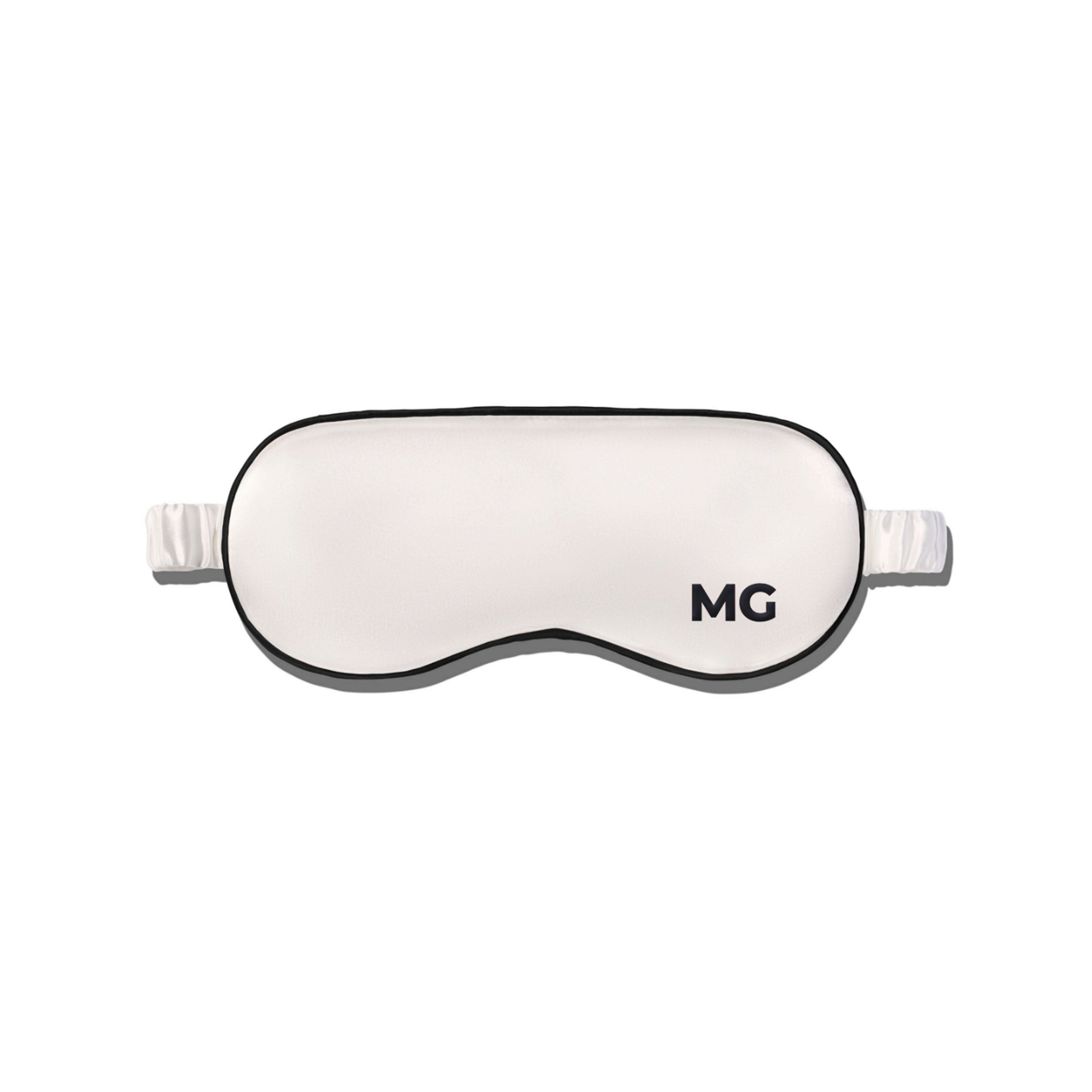 A white silk sleep mask with the initials 'MG' embroidered on the front.