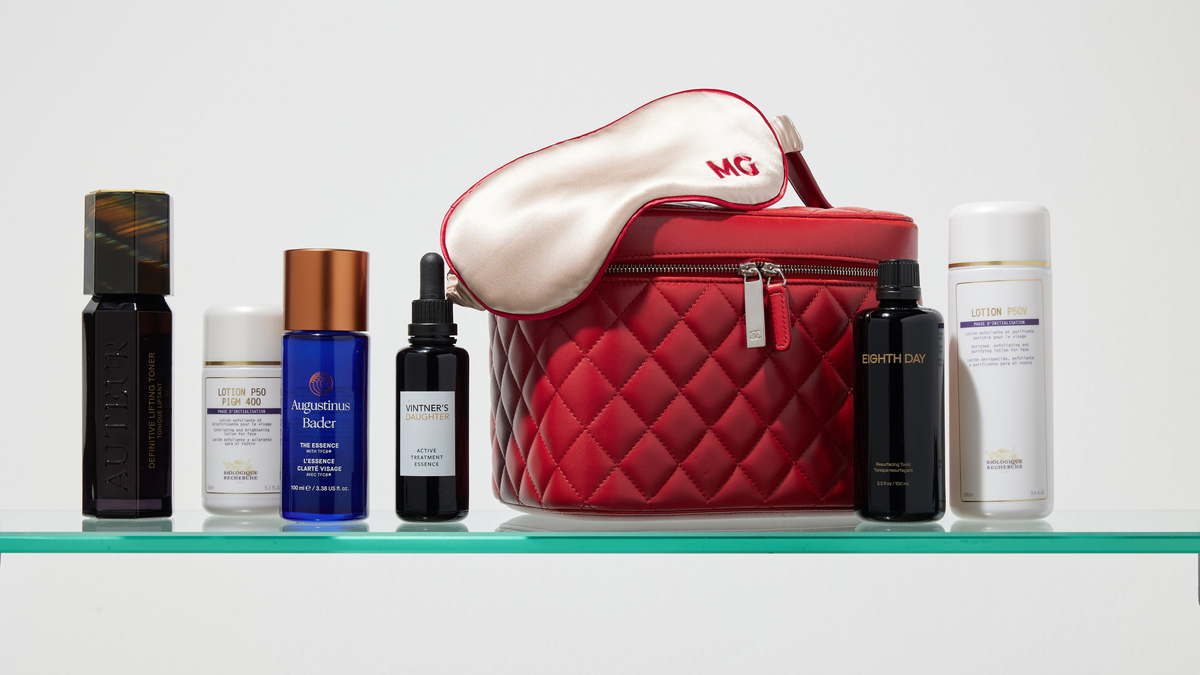 Skincare bottles, a silk MG sleep mask and a red travel case on a glass shelf