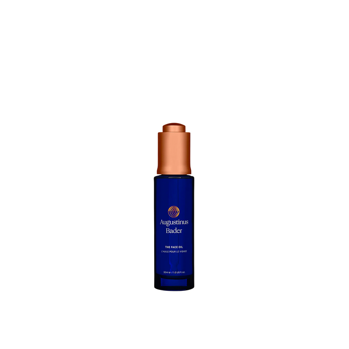 A bottle of Augustinus Bader The Face Oil with a blue label and a copper-colored cap.