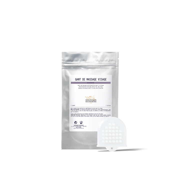 A packaged facial massage glove with a white and purple label, and an additional white glove with a textured surface lying in front.