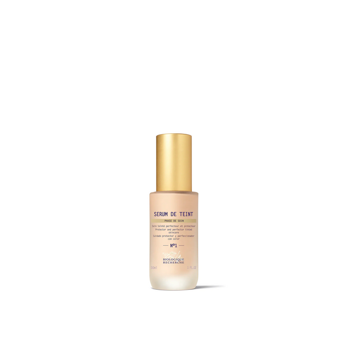 A bottle of Biologique Recherche Serum de Teint with a gold-colored cap and a white label, designed for even skin tone and hydration.