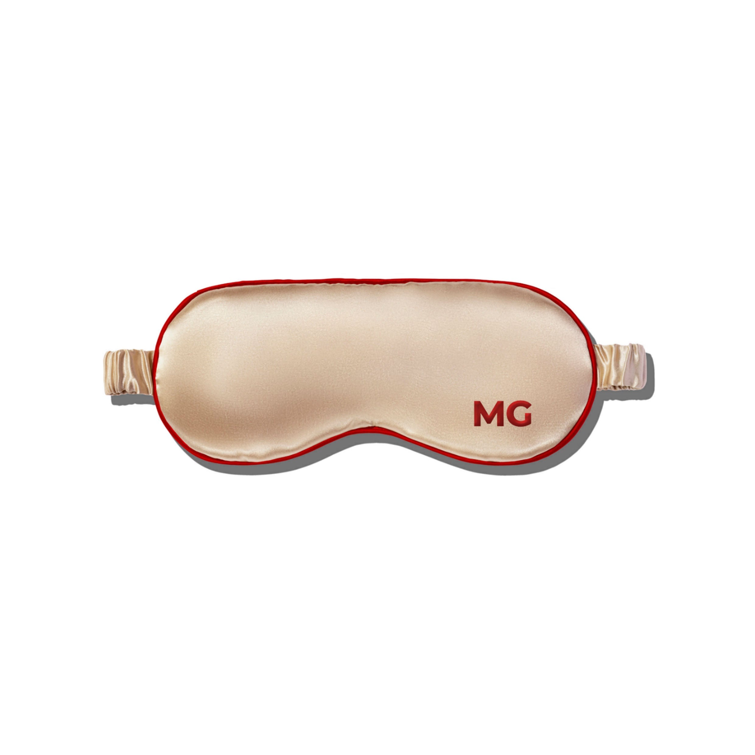 A champagne silk sleep mask with the initials 'MG' embroidered on the front.
